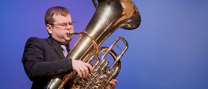Kopermuzikant bespeelt een grote tuba tegen een blauwe achtergrond